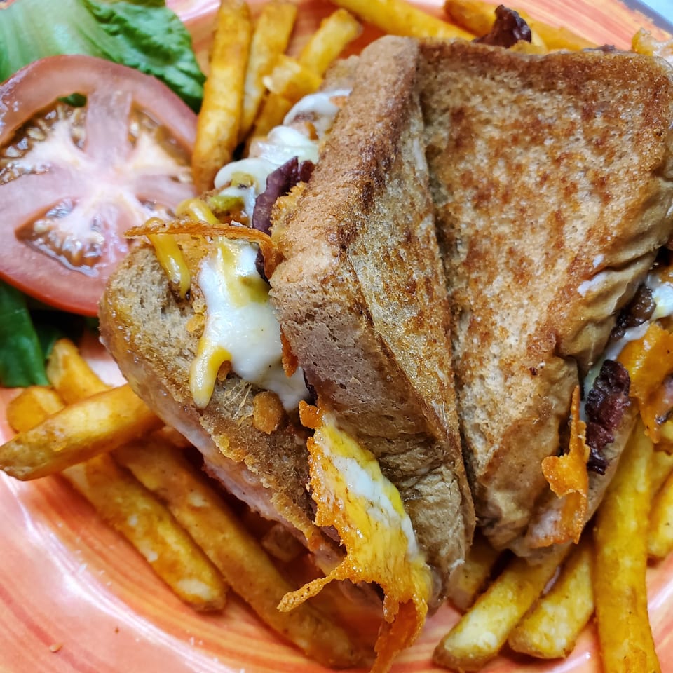 A grilled cheese sandwich with melted cheese, fries, and a side salad with tomato and lettuce.