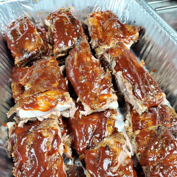 Close-up of juicy, saucy BBQ ribs in a foil pan, ready to be served.
