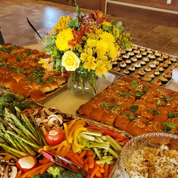 A buffet table laden with sliders, vegetable platters, and small appetizers, adorned with a yellow floral centerpiece.