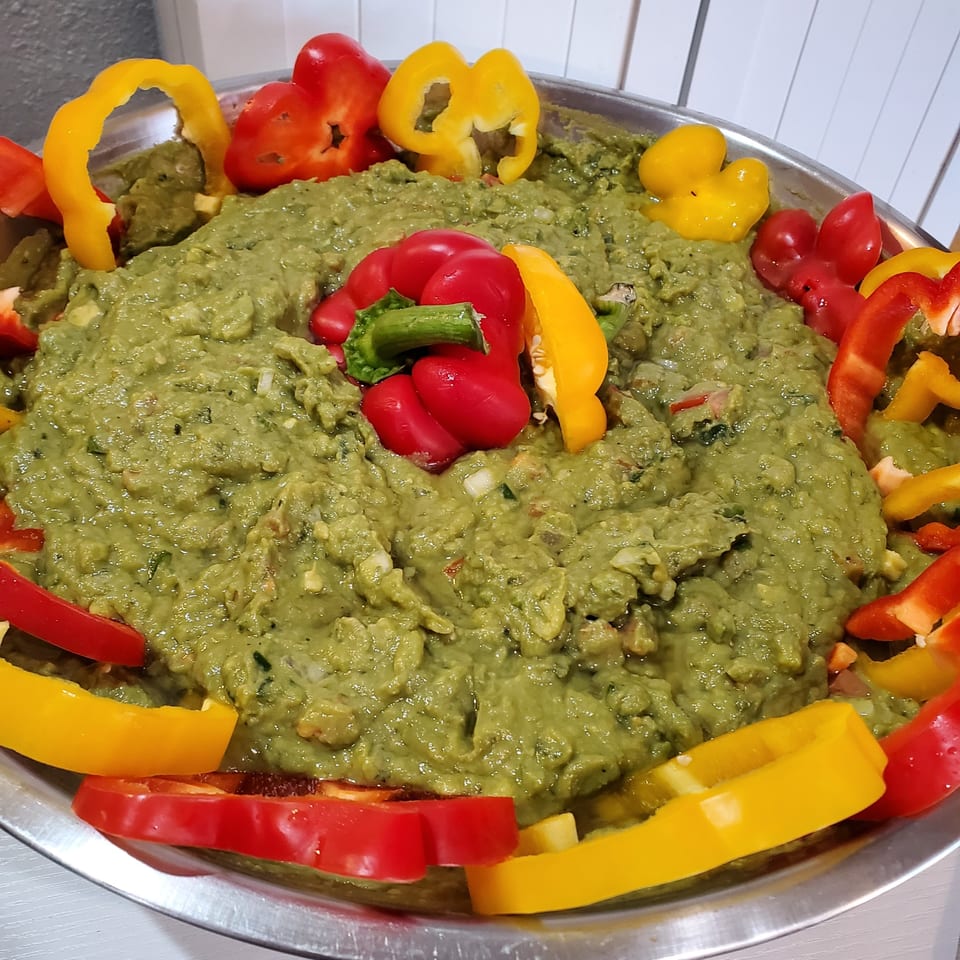Large bowl of guacamole garnished with red and yellow bell pepper slices.