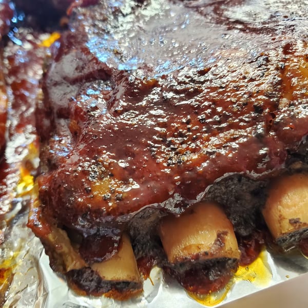 Close-up of glistening BBQ ribs with dark sauce and visible bones, resting on aluminum foil.