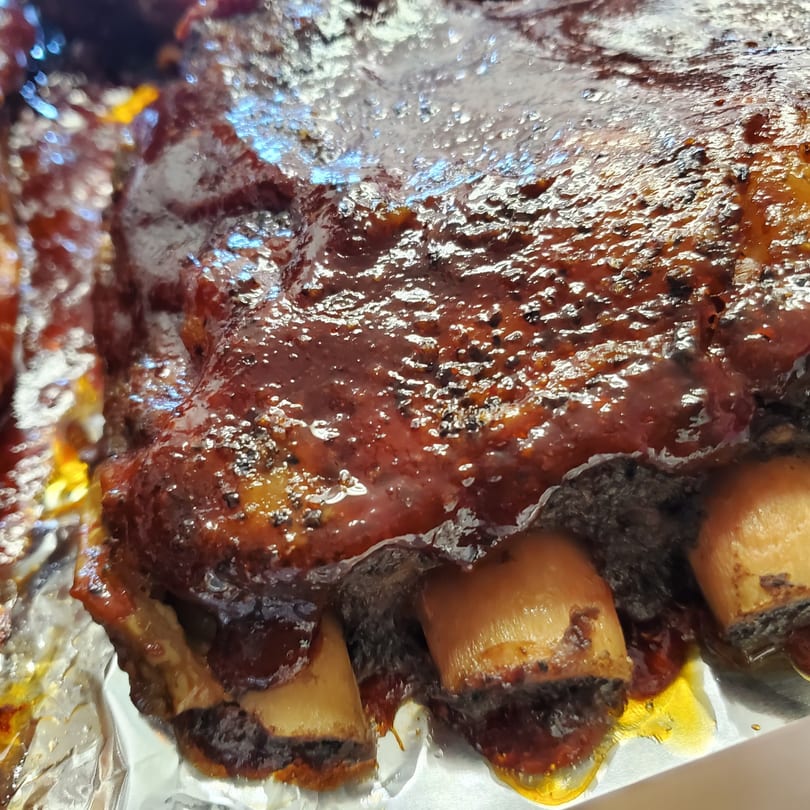 Close-up of glistening BBQ ribs with dark sauce and visible bones, resting on aluminum foil.