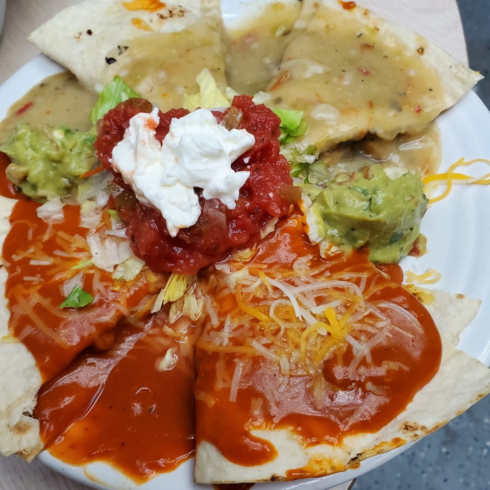 A plate of quesadillas topped with red sauce, cheese, salsa, sour cream, and guacamole.