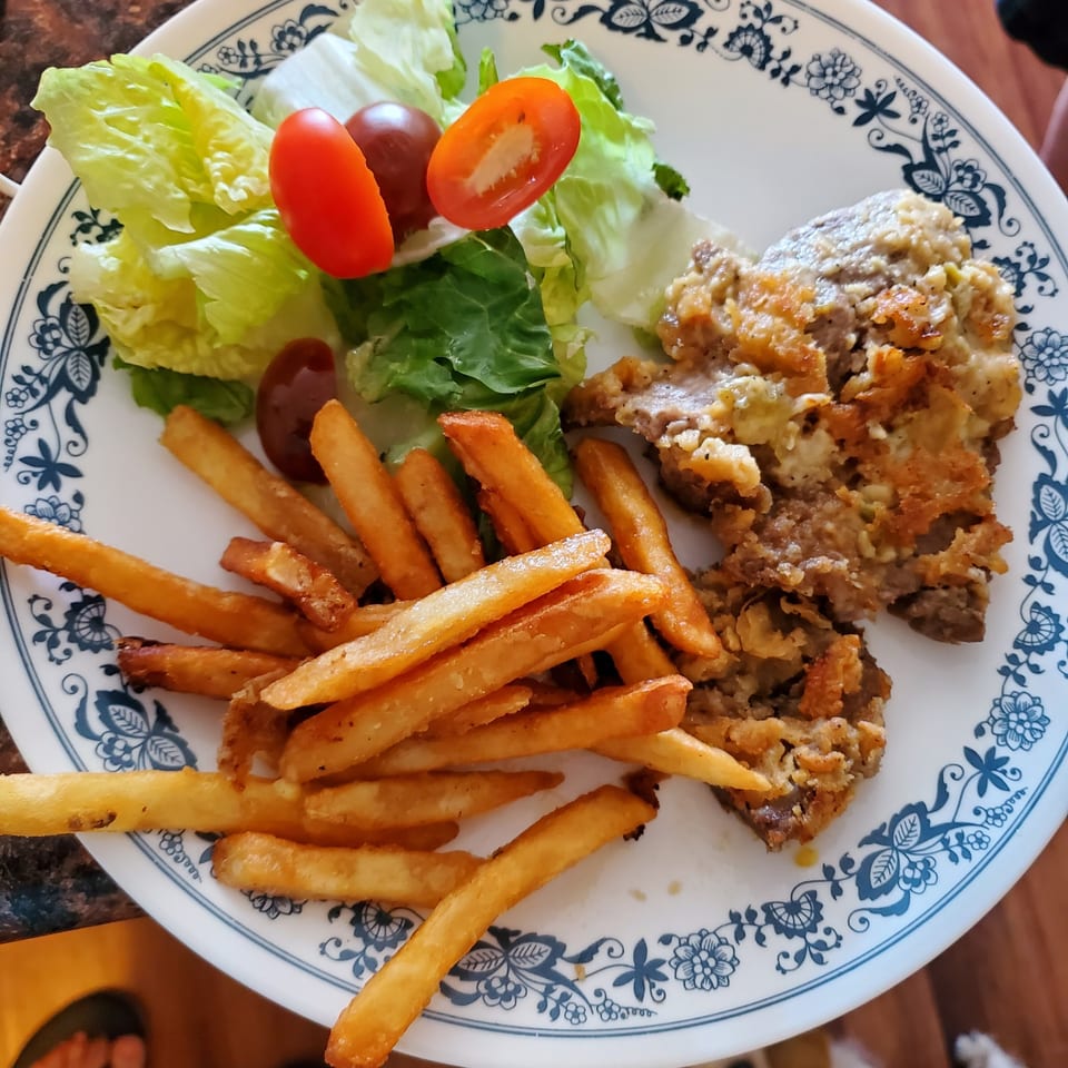 A plate of chicken fried steak, french fries, and a side salad with cherry tomatoes.