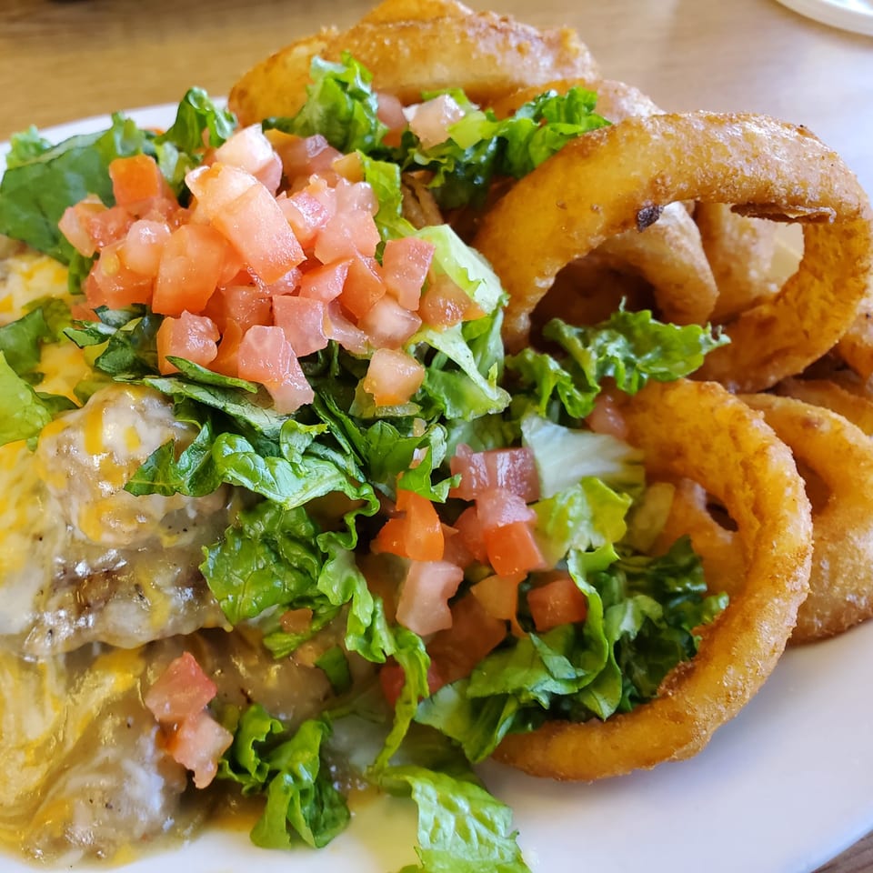A close-up of a dish with melted cheese, lettuce, diced tomatoes, and crispy onion rings.
